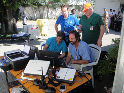 Physicians sitting at a desk outside looking at a monitor