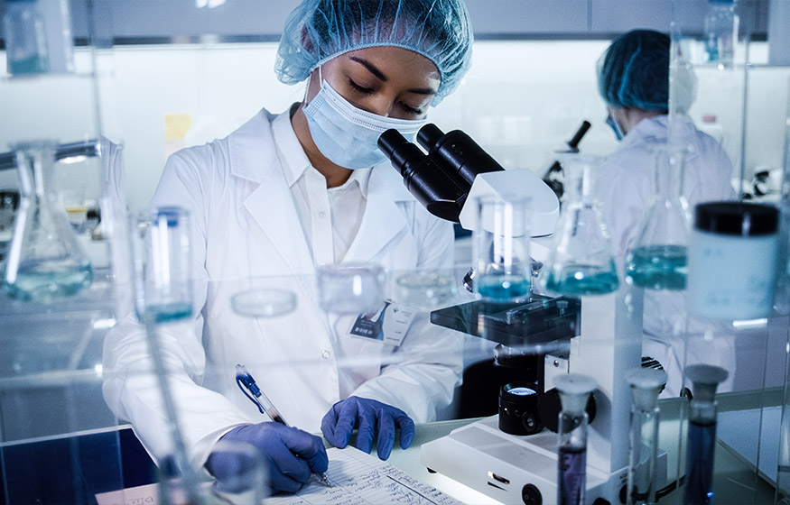 Multi ethnic, female team studying DNA mutations. Using microscope in protective workwear