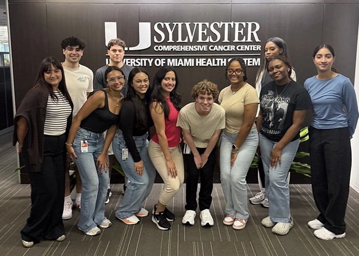 students pose for a grou pphoto infront of the Sylvester Logo