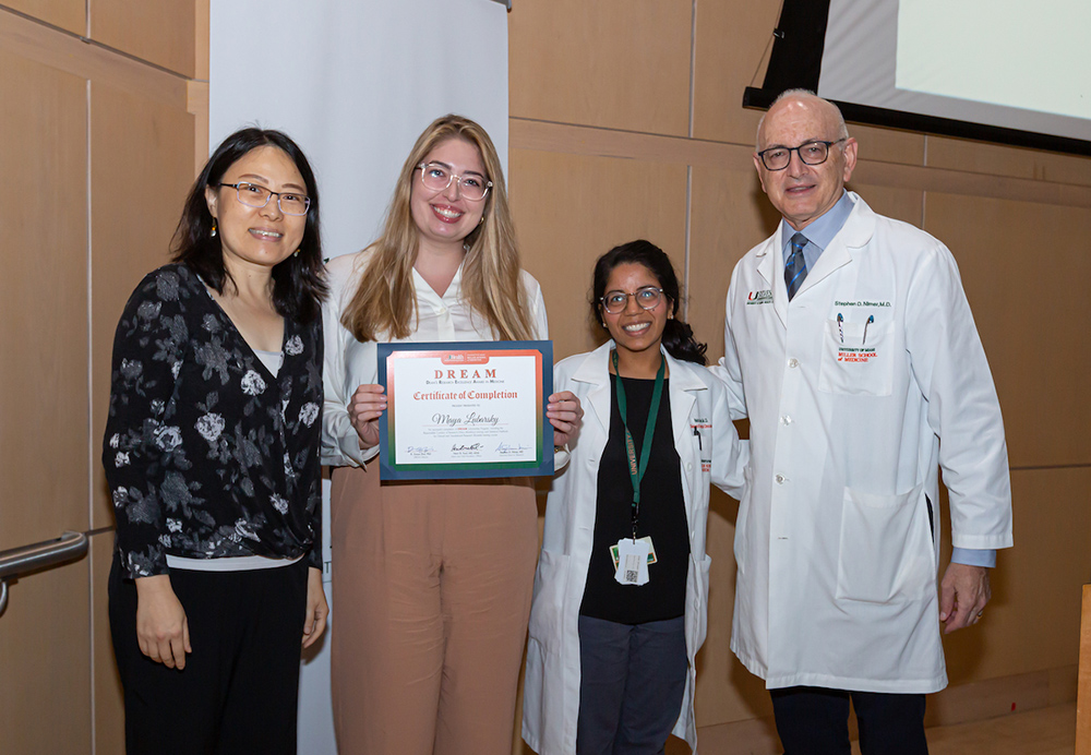 Four people posing with a DREAM certificate two wearing white medical coats