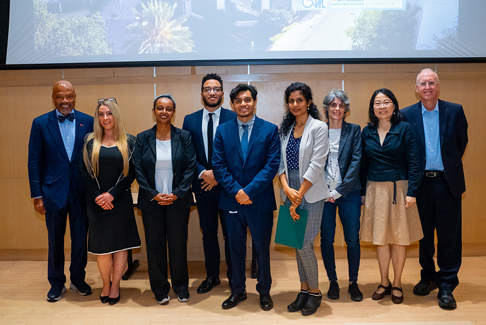 Group photo of DREAM participants and faculty standing in front of a large screen