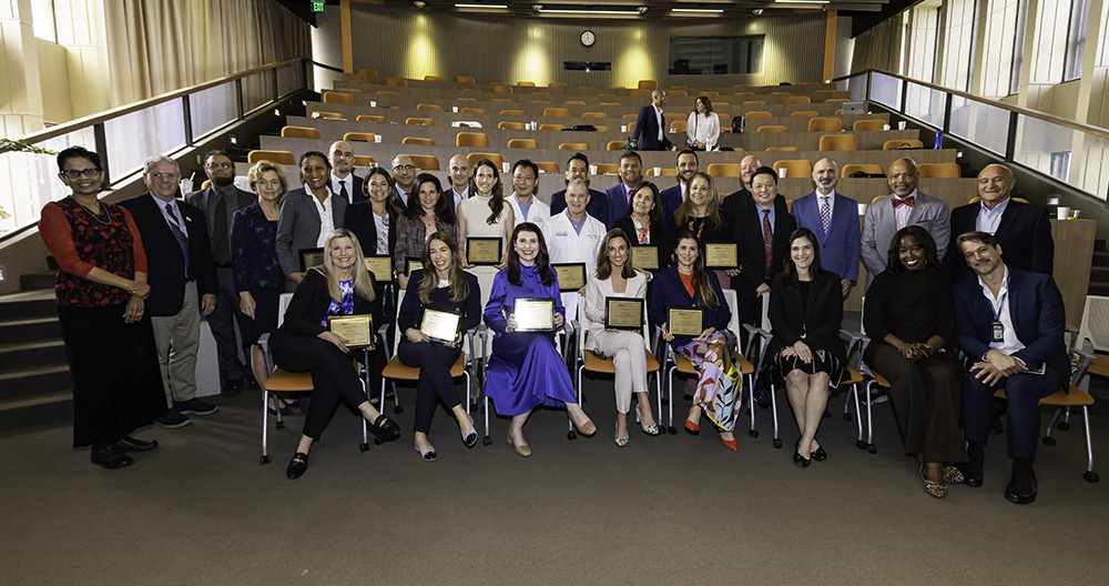 Large group of people in an auditorium holding plaques and smiling