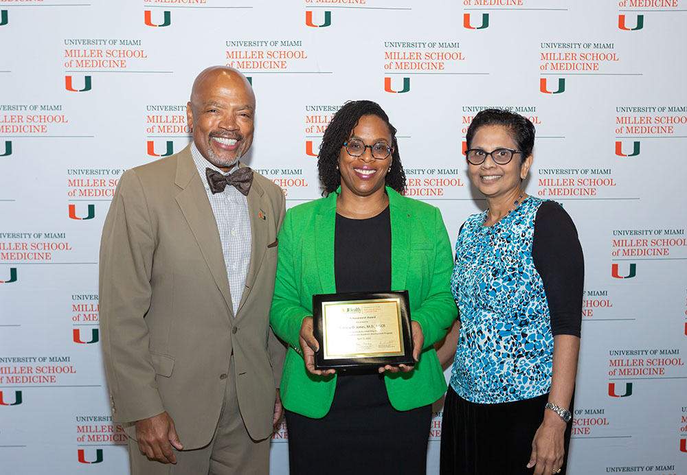 Three people posing with award plaque in front of Miller School backdrop