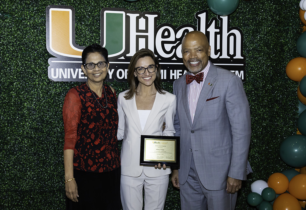 Three people posing with award plaque in front of UHealth backdrop