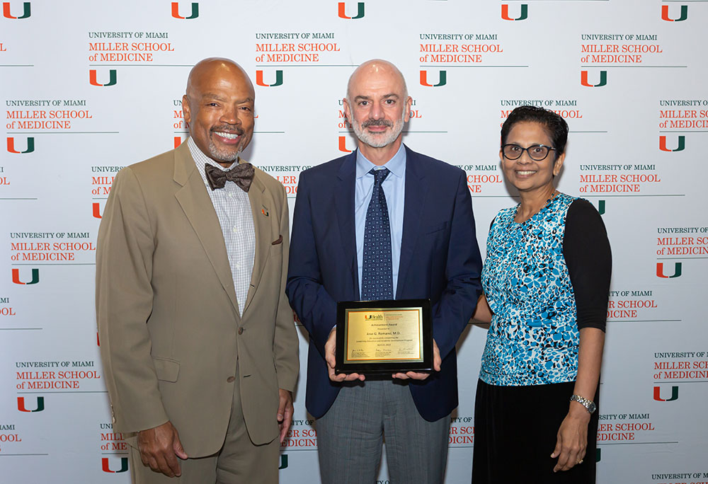 Three people smiling with award plaque in front of Miller School backdrop