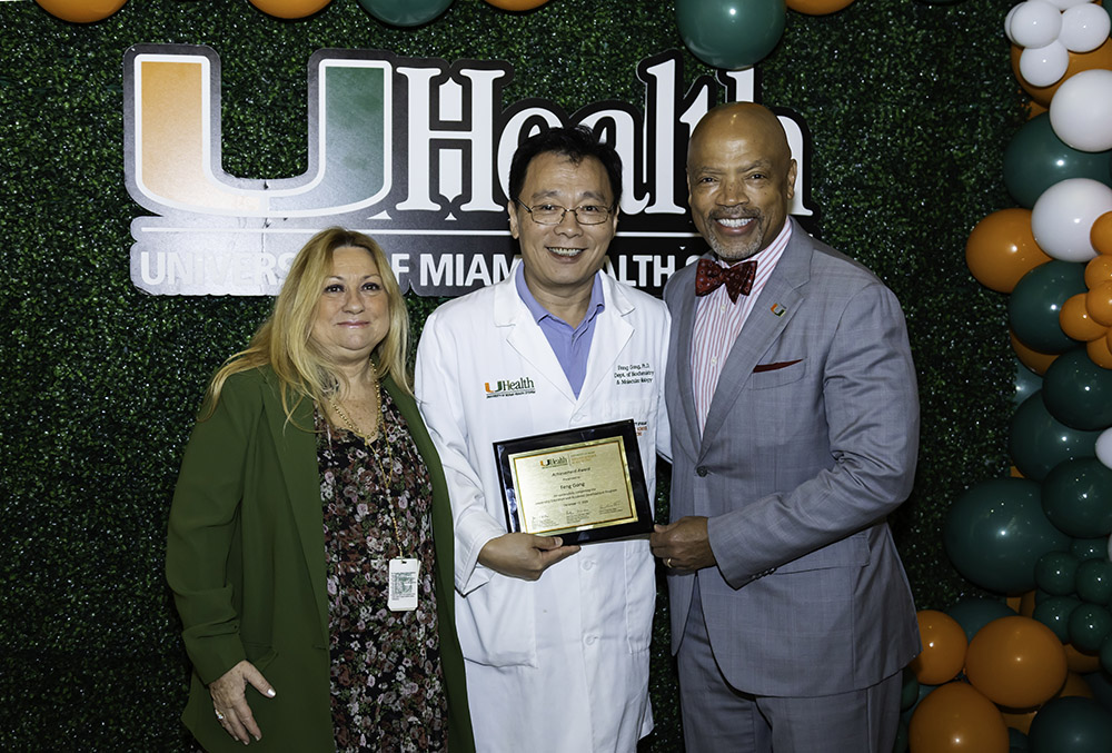 Three people smiling with award plaque in front of UHealth backdrop