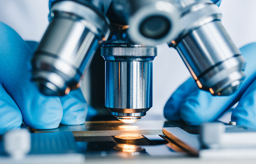 Closeup shot of a technician with blue latex gloves who is operating a microscope