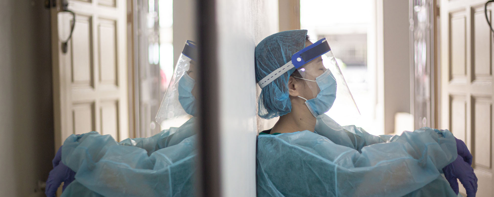 A masked doctor leaning against a wall in exhaustion